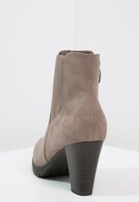 Grå mocka ankelsko med hög klack, med elastiska sidopaneler och rund tå. Inkluderar en dekorativ knapp på baksidan.