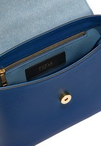 Borsa a tracolla in pelle blu con texture, chiusura a bottone dorato, pattina aperta che mostra una tasca interna con zip e etichetta del marchio Furla all'interno.