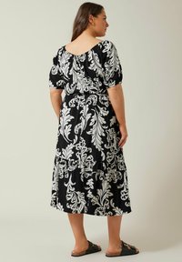 Vestido negro con estampado floral blanco, mangas cortas abullonadas, escote trasero fruncido, falda en capas y combinado con sandalias negras.
