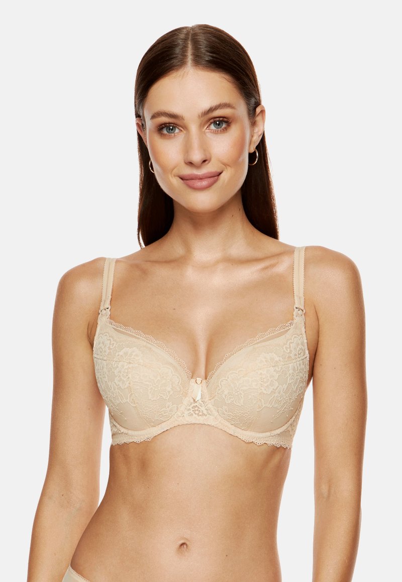 Beżowy biustonosz z koronką, ozdobiony kwiatowymi wzorami, z fiszbinami, regulowanymi ramiączkami i dekoracyjną kokardką na środku. Gładka tekstura.