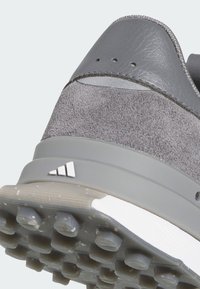 Chaussure de sport grise avec dessus en daim et cuir, détails texturés, et semelle extérieure en caoutchouc à motif antidérapant. Accentuée d'un logo.