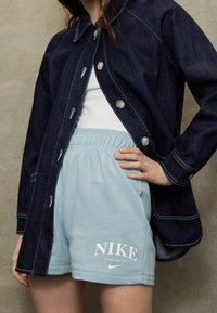 Denim jacket with button closure and light blue cotton shorts featuring a white "NIKE" graphic and elastic waistband.