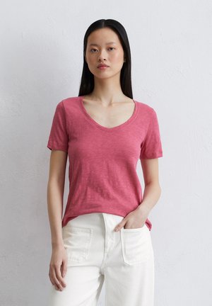 Rosa kurzärmliges V-Ausschnitt-T-Shirt aus leichtem Stoff; hat eine entspannte Passform und eine dezente Textur. Kombiniert mit weißen Hosen.