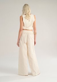 Top corto color crema e pantaloni larghi a righe verticali, realizzati in tessuto leggero; presentano una vita elastica.