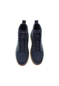 Ett par marinblå U.S. Polo Assn. snörade stövlar med bruna sulor seddes uppifrån på en vit bakgrund.