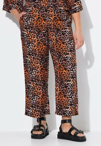 Leopardprint wijde broek in oranje, zwart en beige stof met een gladde textuur, gecombineerd met stevige zwarte sandalen met dikke banden.