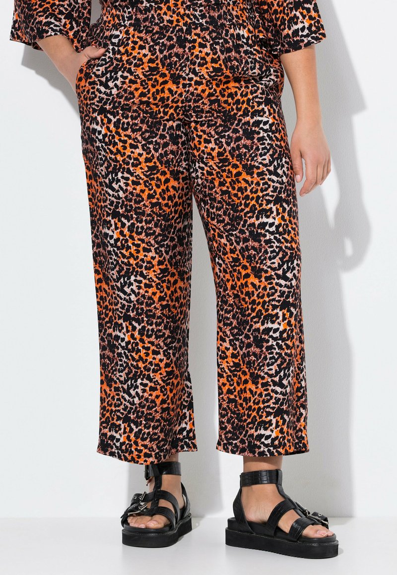 Leopardprint wijde broek in oranje, zwart en beige stof met een gladde textuur, gecombineerd met stevige zwarte sandalen met dikke banden.