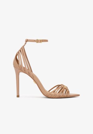 Bež otvorena sandala na visoku petu s više tankih remenčića, kopčom oko gležnja i tankom štiklom, okrenuta u lijevu stranu na bijeloj pozadini.