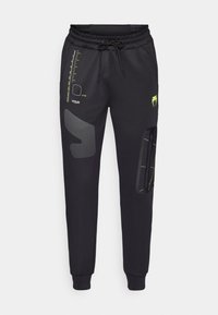 Sorte joggers lavet af blødt stof, med mesh-detaljer, snor i taljen og gule grafik, herunder et logo og målerdesign.