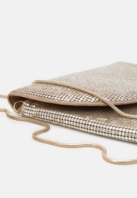 Sac en maille métallique avec un design plié, présentant une texture lisse et brillante ainsi qu'une fine bandoulière à chaîne spirale. Les couleurs incluent des accents dorés et argentés.