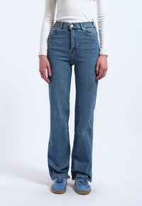 Hellblaue High-Waist-Jeans mit geradem Beinschnitt, ausgestattet mit einem klassischen Knopf- und Reißverschluss und sanften Verwaschungen auf dem Stoff.