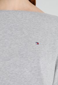 Gray cotton sweatshirt with a wide neckline and small designer logo in red, white, and blue on the left side. Soft texture and casual design.