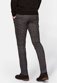 Spodnie w kratę w brązowo-granatową kratę, o dopasowanym kroju, z lekkiego materiału, o gładkiej fakturze i wąskich nogawkach, zestawione z ciemnymi butami.