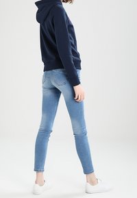 Navy hoodie with a kangaroo pocket, paired with light blue skinny jeans that have a faded effect, and white slip-on sneakers.