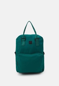 Sac à dos en tissu turquoise avec deux poignées supérieures, une poche zippée à l'avant et une forme rectangulaire. Présente un patch logo noir à l'avant.
