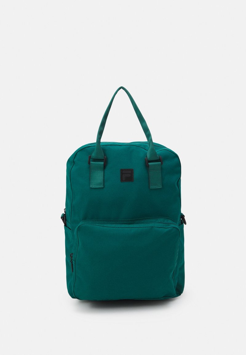 Sac à dos en tissu turquoise avec deux poignées supérieures, une poche zippée à l'avant et une forme rectangulaire. Présente un patch logo noir à l'avant.