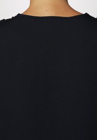 Černý oděv s měkkou, strukturovanou tkaninou; má kulatý výstřih a jednoduchý design. Bez viditelného kování nebo vzorů. Pohled zezadu.