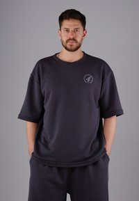 Dunkelgraues, übergroßes Sweatshirt mit kurzen Ärmeln, rundem Halsausschnitt und einem Logo auf der Brust. Hergestellt aus weichem, strukturiertem Stoff.