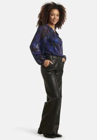 Flowy blue and black patterned blouse with long sleeves, paired with high-waisted black faux leather pants and pointed black heels.