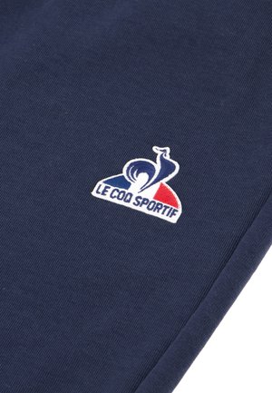 Navy blue fabric features a white embroidered logo with red and blue accents, displaying a stylized rooster and the text "LE COQ SPORTIF."