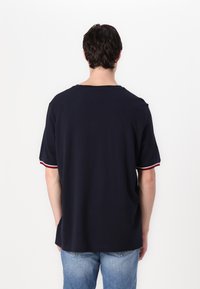 Marineblå bomulds t-shirt med korte ærmer, der har røde og hvide stribede detaljer ved ærmeafslutningerne. Lige kant og løstsiddende pasform.