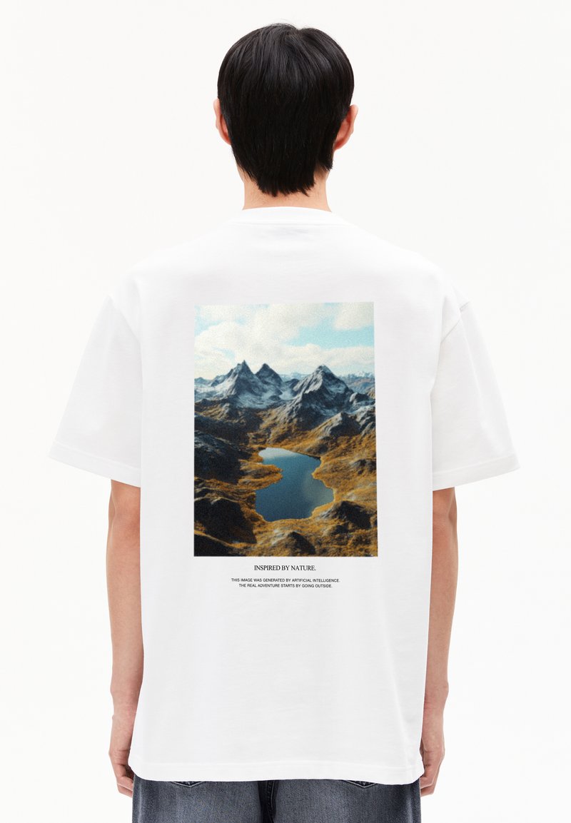 T-shirt blanc avec un imprimé graphique de montagnes et d'un lac au dos, avec le texte "Inspiré par la Nature" en dessous de l'image.