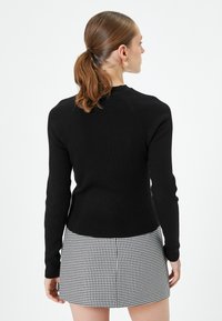 Czarny sweter ryfli z długimi rękawami, dopasowany krój i wysoki dekolt, w połączeniu z mini spódnicą w czarno-białą kratę w zęby psa.