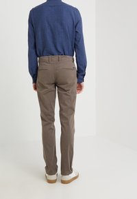 Bruna chinos i bomull med rak benpassform, två bakfickor och subtila sömmar, tillsammans med en blå långärmad skjorta.