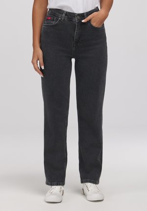 Kobieta nosząca czarne, proste jeansy z wysokim stanem i przednimi kieszeniami, w połączeniu z białymi trampkami i włożoną białą koszulą.