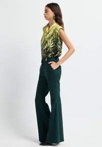 Groen met bladerenpatroon mouwloos topje met een colhals; hooggetailleerde donkergroene flared broek met een gouden accent op de riem.