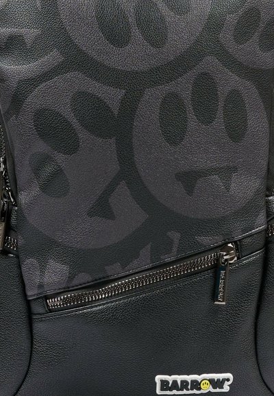 Zwarte leren rugzak met een gestructureerd oppervlak en een subtiele matte afwerking, omlijnde ritsen en een logotag rechtsonder.