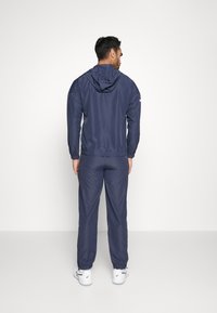 Navy tracksuit with a hooded jacket and elastic cuffs. Smooth, lightweight material; fitted design; jogger-style pants with tapered legs.