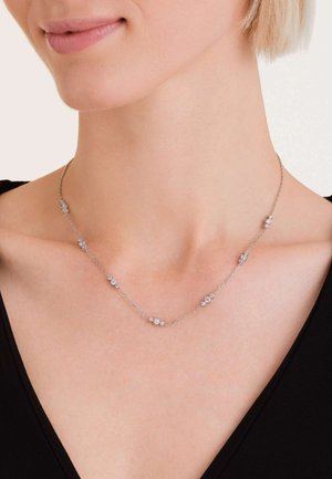 Collana in argento con piccoli accenti rotondi e a forma di fiore, con una finitura liscia e un design delicato, indossata attorno al collo.