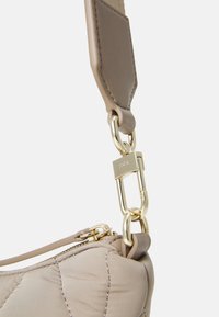 Tira de bolso acolchada color beige con herrajes en tono dorado y un cierre de clip, con una textura suave y una silueta blanda.
