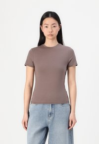 Brun kortermet t-skjorte med rund hals, laget av glatt stoff, passformen er tettsittende, kombinert med lyseblå løstsittende jeans.