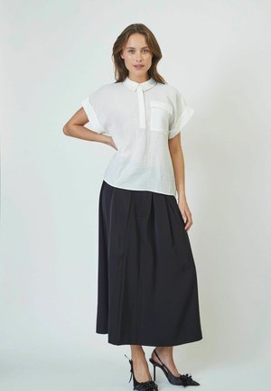 White short-sleeve top with collar and front pocket, paired with a black pleated maxi skirt, worn with black heeled shoes.