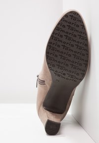 Beige Wildleder-Wristboots mit einem seitlichen Reißverschluss, ausgestattet mit einer strukturierten schwarzen Sohle, auf der "Tamaris" geprägt ist, und einem flachen Absatz.