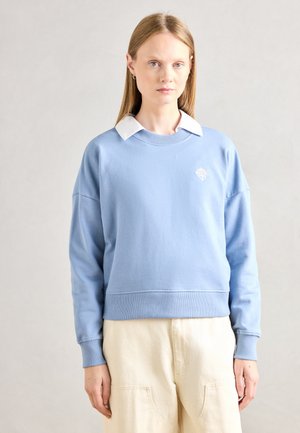 Felpa azzurro chiaro con scollo a girocollo, polsini e orlo a coste. Presenta una camicia bianca con colletto sotto e un logo ricamato.