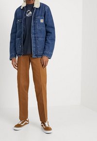 Jeansjacka med krämfärgad pälskrage, marinblå t-shirt, bruna chinos och bruna sneakers med vita detaljer. Avslappnad lager-på-lager outfit.