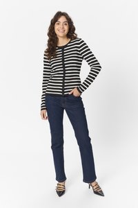 Gilet rayé noir et blanc avec un devant à boutons, associé à un jean bleu foncé et des escarpins noirs à bout pointu. Tissu lisse et design ajusté.