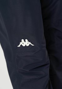 Marina blå träningsbyxor gjorda av slätt tyg, med en vit Kappa-logotyp. Designen inkluderar diskret sömnad och en avsmalnande passform.