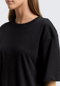 Zwarte katoenen T-shirt met korte mouwen en een ronde halslijn, versierd met een patroon van kleine, glanzende embellissements over de voorkant.