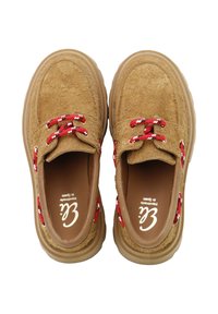 Zapatos de ante color beige con puntera redonda. Cuentan con cordones trenzados en rojo y blanco y una suela de goma marrón. Parte superior texturizada para mayor agarre.