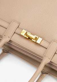 Sac à main en cuir beige avec une surface texturée, des poignées doubles et un fermoir en métal doré. Présente une ouverture à glissière sur le côté.