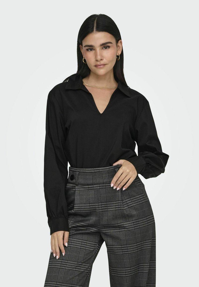 Blusa nera a maniche lunghe con scollatura a V e polsini con bottoni, abbinata a pantaloni a palazzo grigi con motivo a quadri e vita alta, dotati di tasche laterali.