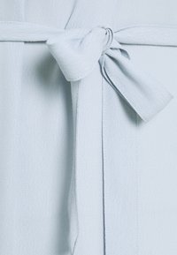 Tejido azul claro con un acabado texturizado, que presenta un detalle de cinturón atado. Caída suave y acentos de diseño minimalista.