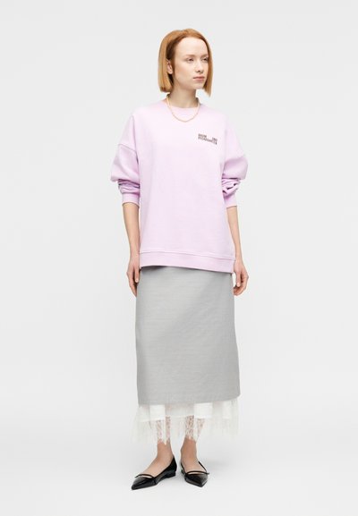 Ροζ ανοιχτόχρωμο φούτερ με ριγμένους ώμους και διακοσμητικό κείμενο, συνδυασμένο με γκρι στενή φούστα με άσπρο δαντελωτό τελείωμα και μαύρα μπαλαρίνα παπούτσια.