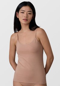 Camisole color nude con spalline sottili, realizzata in morbido tessuto a costine, con scollatura a girocollo e design aderente.