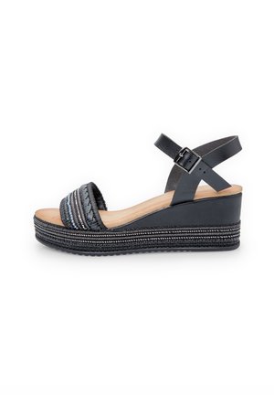 Sandale compensée noire avec une bride tissée texturée, une bride de cheville en cuir avec boucle et une semelle de style espadrille à motif.