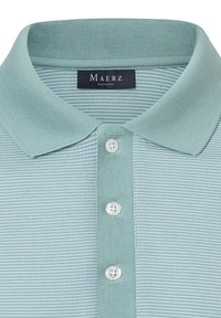 Ljusblå polo skjorta med en texturerad framtill, som har en ribbad krage, tre knappar i placket och en tryckt varumärkesetikett vid halsen.